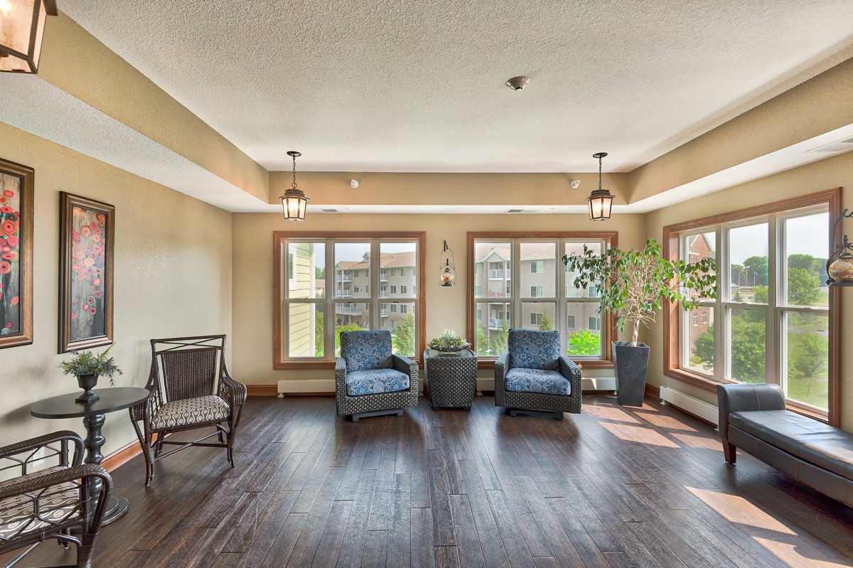 A bright living room with large windows, featuring two blue chairs, a small table, and plants.