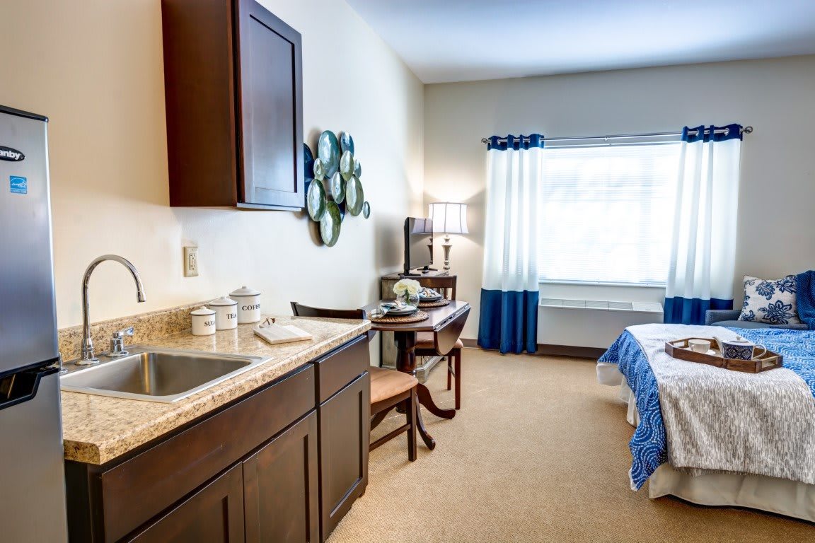 A cozy bedroom with a small kitchenette and window.