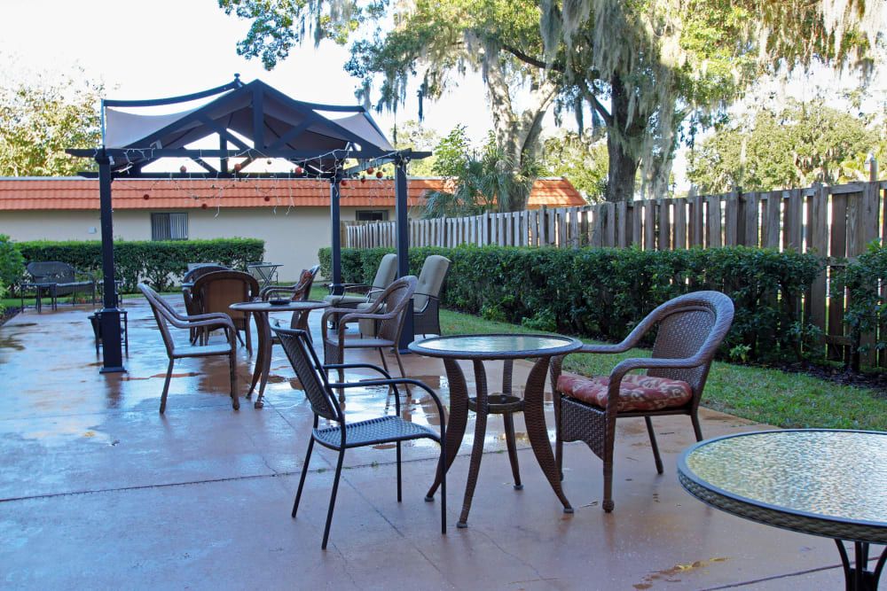 A sunny outdoor patio with tables and chairs set up under a gazebo, surrounded by trees.