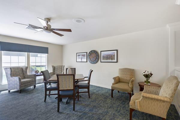 A well-decorated living and dining area featuring a round table with chairs, comfortable armchairs, and a ceiling fan.