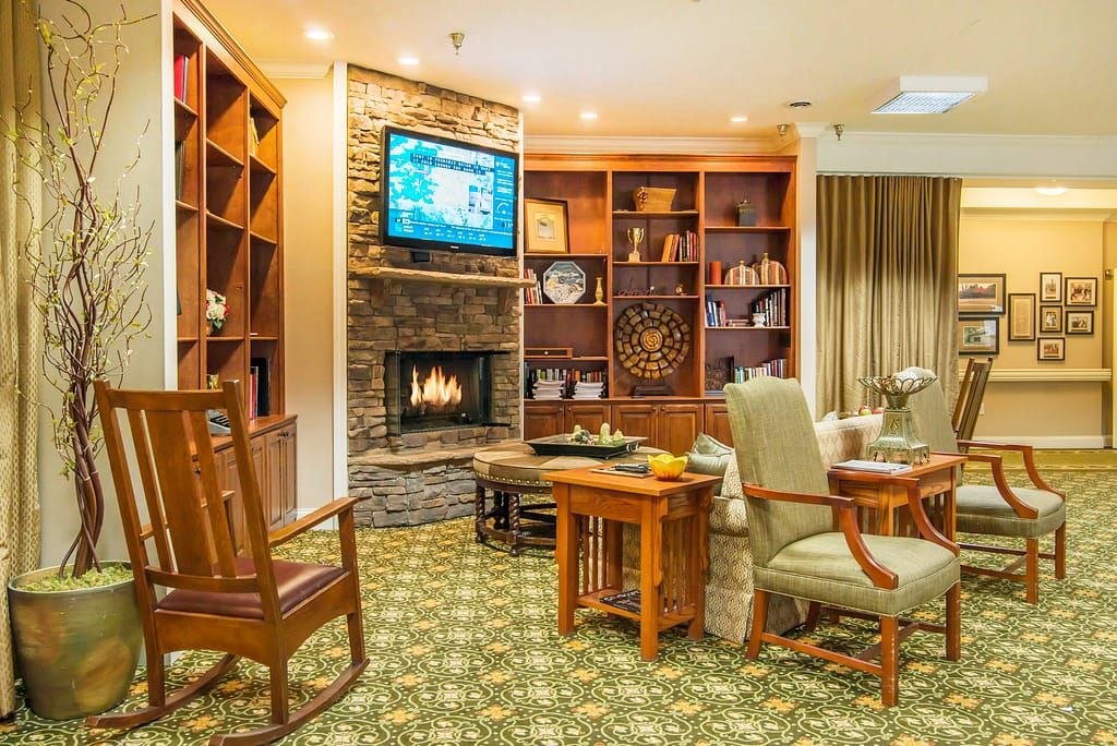 A cozy living room featuring a fireplace, bookshelves, and comfortable seating with a television mounted above the mantel.