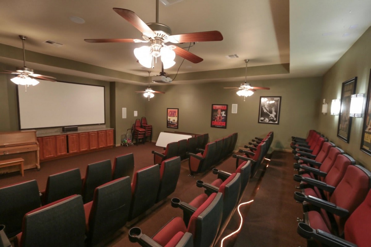 A cozy home theater room with multiple seating rows, ceiling fans, and a projector screen surrounded by movie posters.