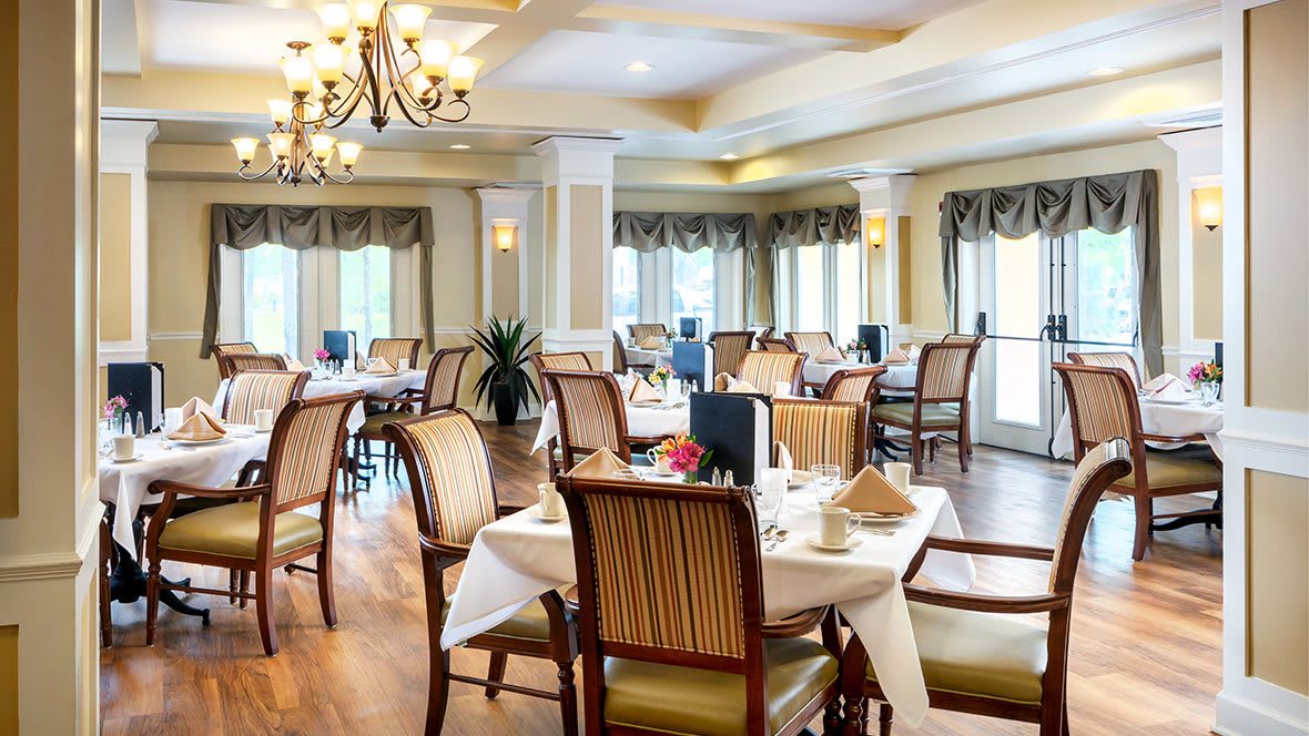 An elegant dining room with neatly arranged tables and chairs, illuminated by a chandelier.