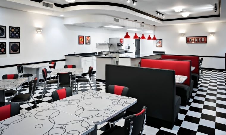 A retro-style diner interior featuring red and black seating with a checkered floor.