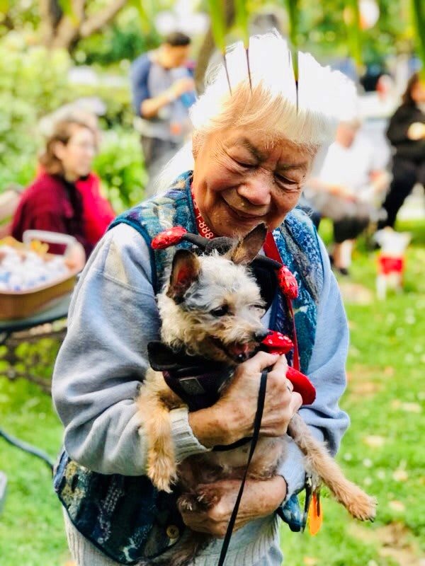 An elderly woman joyfully holding her dog in a park setting.