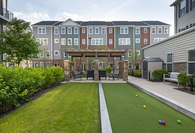 A residential apartment complex featuring a landscaped backyard with a bocce court and outdoor seating area.