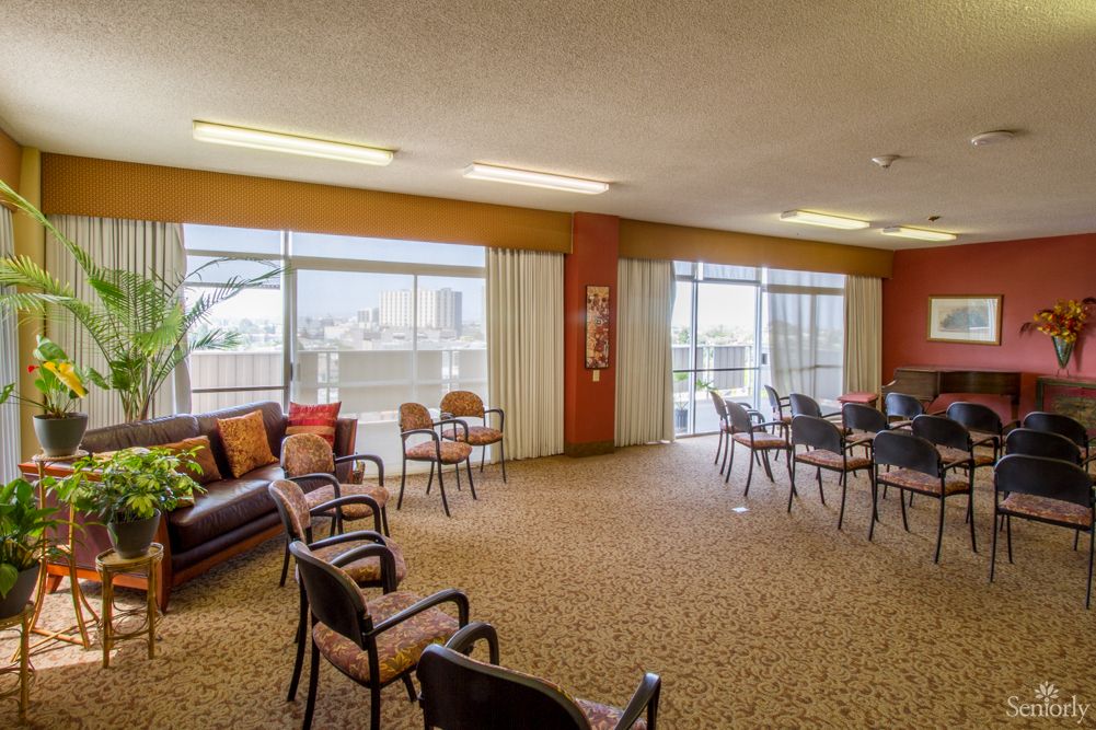 A spacious community room with multiple chairs arranged in a circular formation, featuring large windows that allow natural light to fill the space.