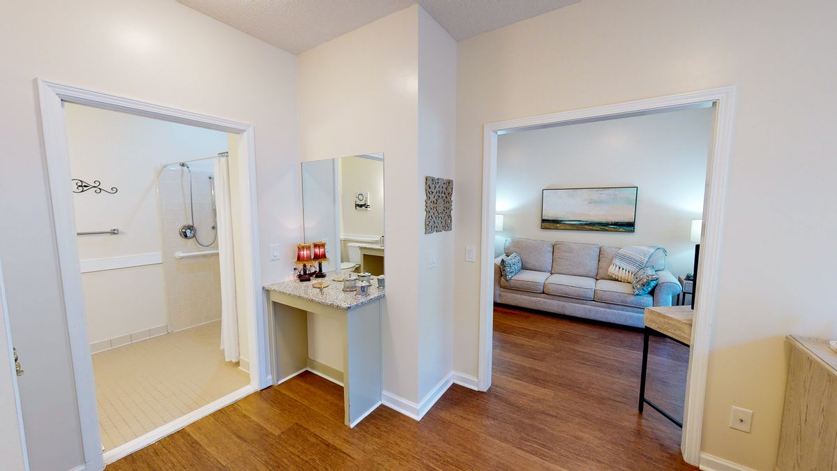 A cozy interior view featuring a living room and bathroom, connected by a hallway with a small vanity area. The space is adorned with simple home decor and hardwood floors.
