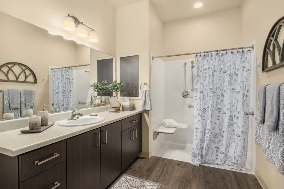 A modern bathroom featuring a large mirror, dark wood cabinetry, and a shower with a patterned curtain.