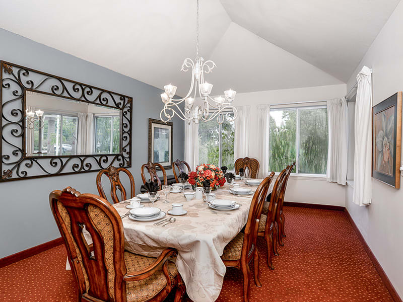 An elegantly set dining room featuring a large dining table with upholstered chairs, accented by a chandelier and a decorative mirror on the wall.
