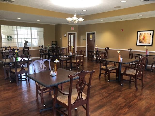 An empty dining room with wooden tables and chairs, featuring a chandelier and wooden flooring.