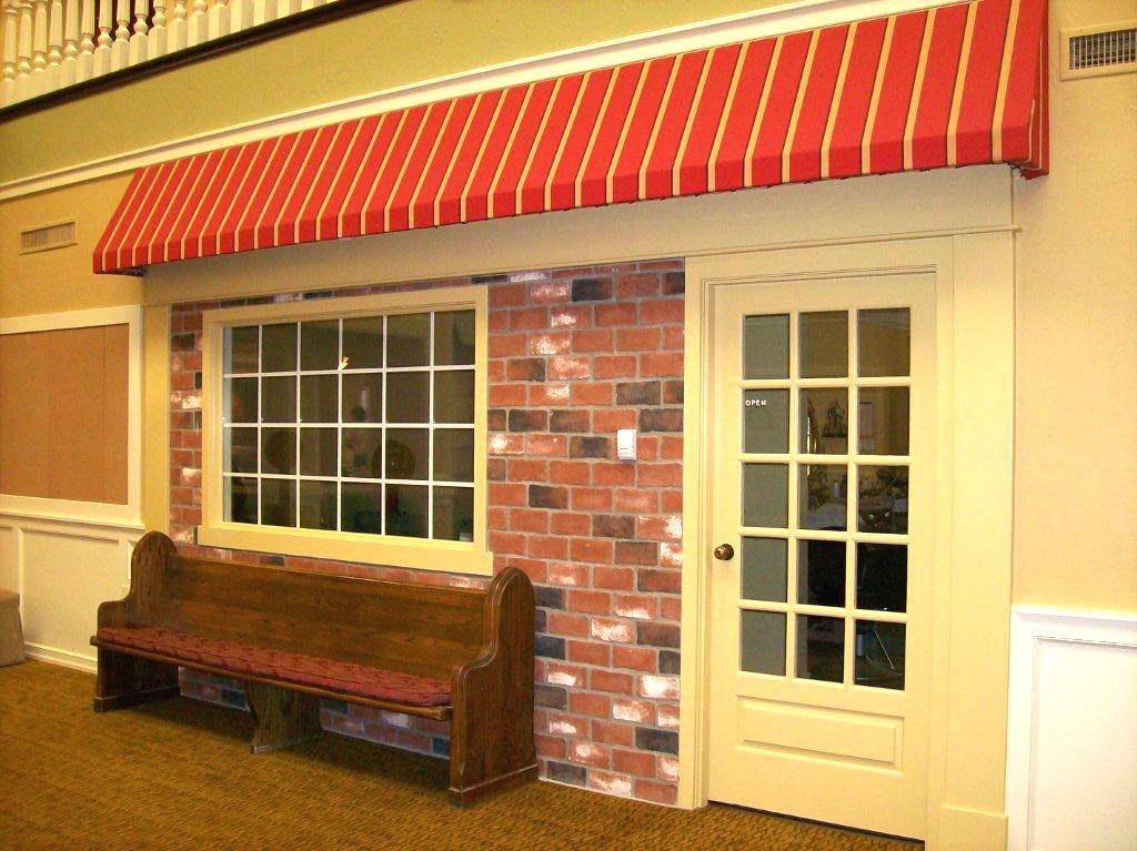 A quaint storefront featuring a red awning, brick facade, and a wooden bench by the glass door.