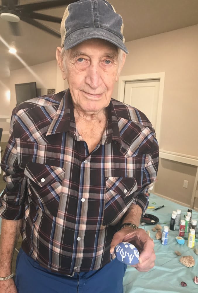 An elderly man wearing a plaid shirt and cap indoors.
