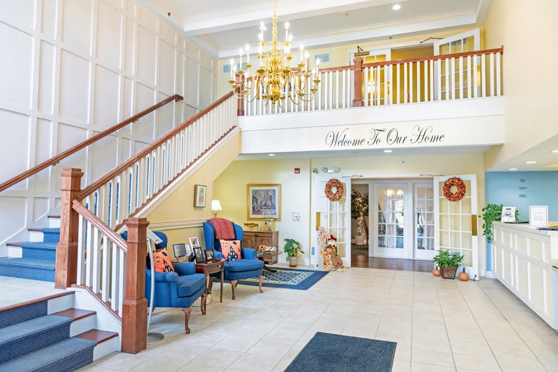 A welcoming lobby with elegant decor, featuring a staircase, chandelier, and comfortable seating.