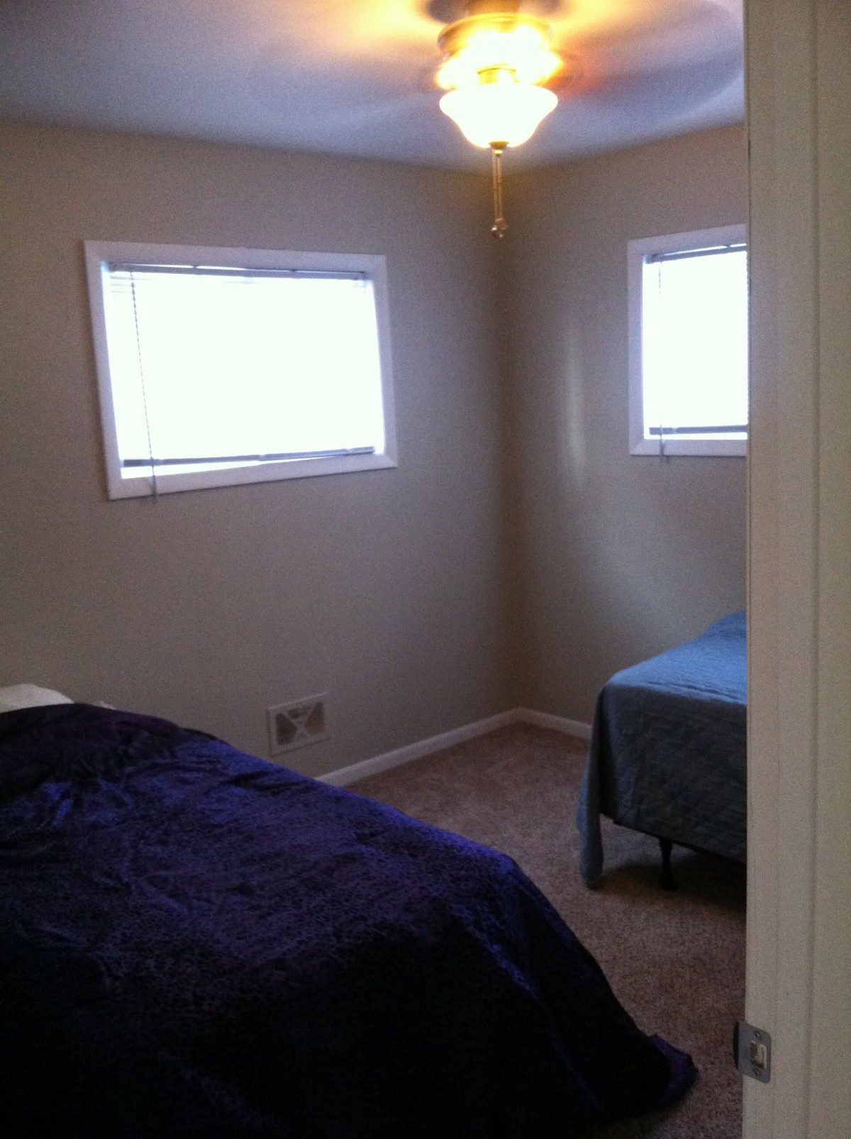 A small bedroom with two beds and two windows, featuring a carpeted floor.