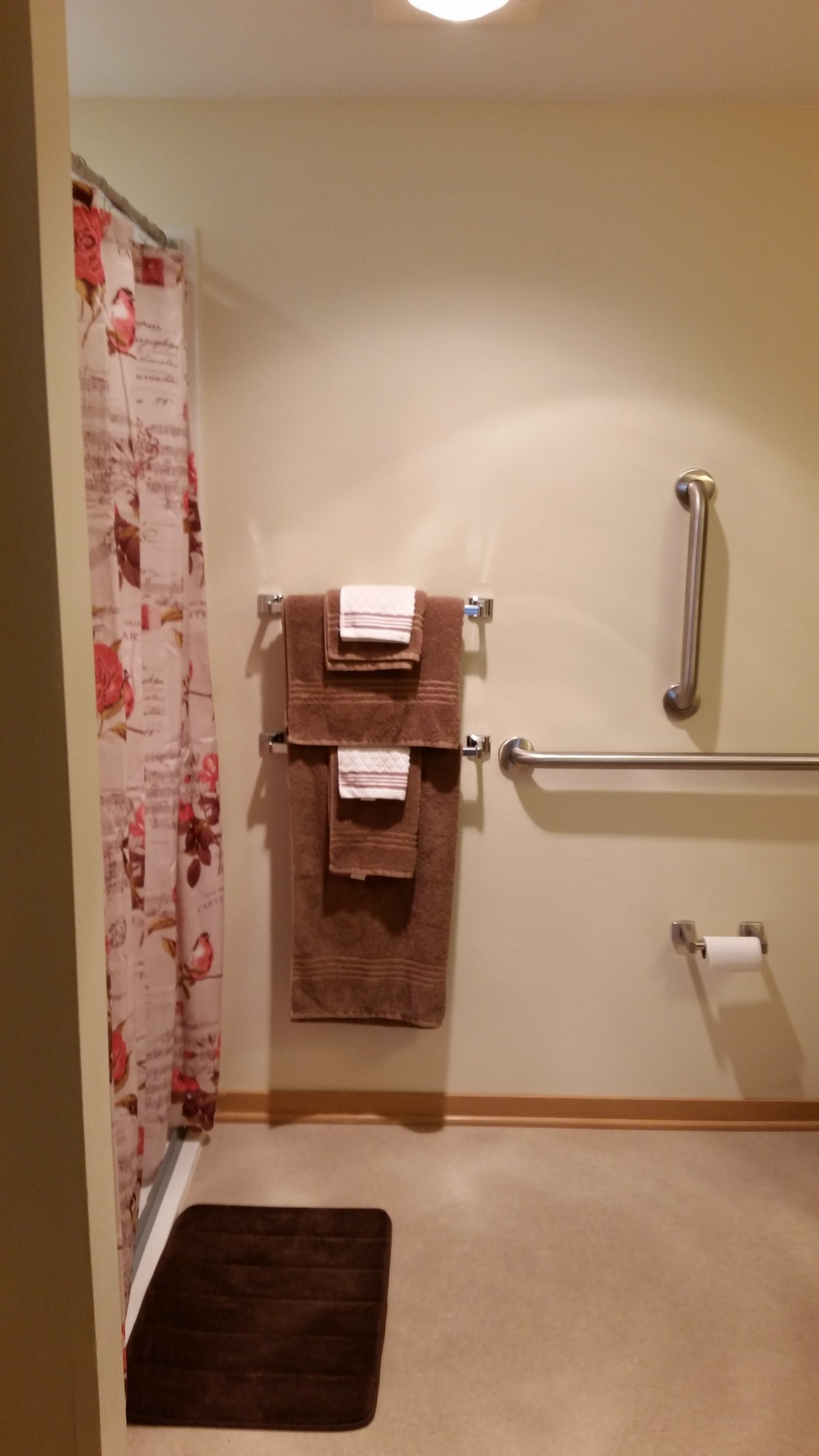A bathroom with neatly hung towels, floral shower curtain, and safety grab bars.