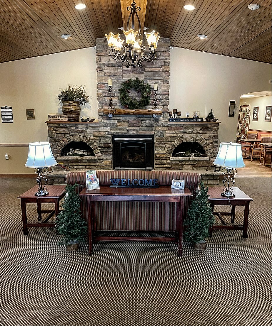 A cozy lounge area with a stone fireplace, flanked by tables and lamps, and decorated with plants.