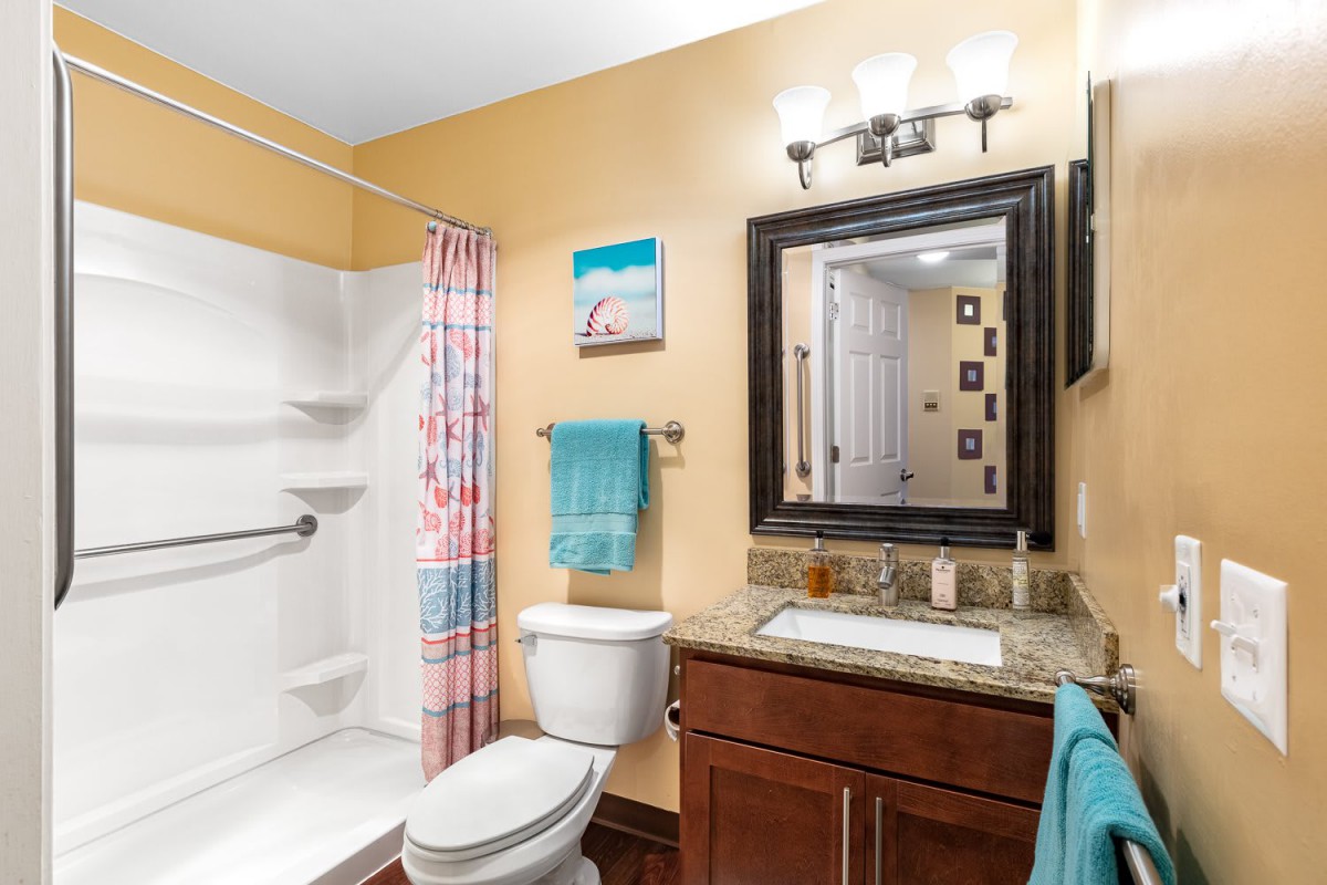 A well-lit bathroom featuring a mirror above a sink, a shower with a curtain, and neatly arranged towels.
