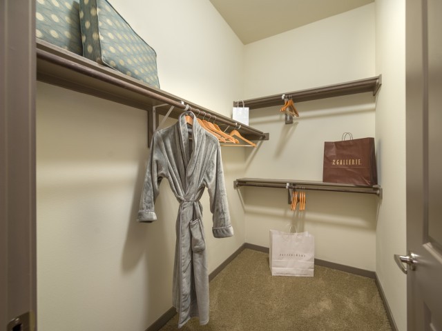 A spacious closet with robes hanging on wooden hangers and shelves for storage.
