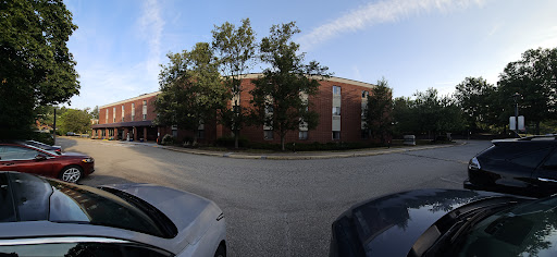 A view of a brick apartment building surrounded by trees with parked cars on the street.