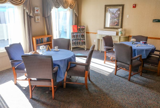 A cozy dining area with round tables covered in blue tablecloths and surrounded by cushioned chairs.