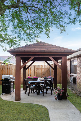 A cozy outdoor gazebo in a backyard, complete with dining furniture and a grill.