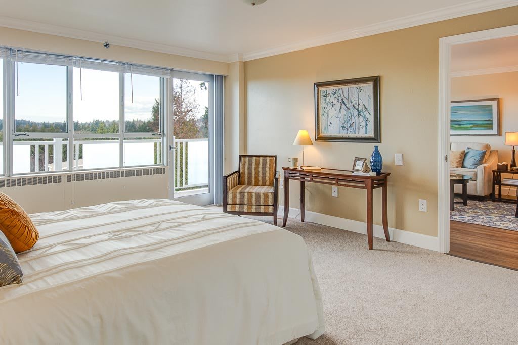 A cozy bedroom with a bed, chair, and a view of the outdoors through a large window.