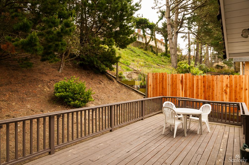 A tranquil outdoor deck area with a table and chairs, surrounded by trees and fenced for privacy.