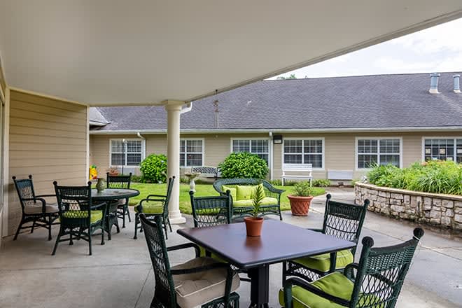A cozy outdoor patio area with tables and chairs, surrounded by a garden and building.