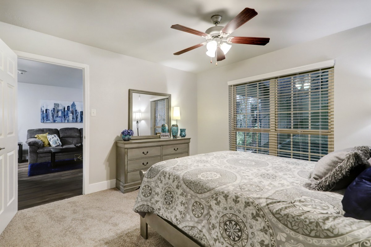A cozy bedroom featuring a bed, dresser with a mirror, and a ceiling fan.