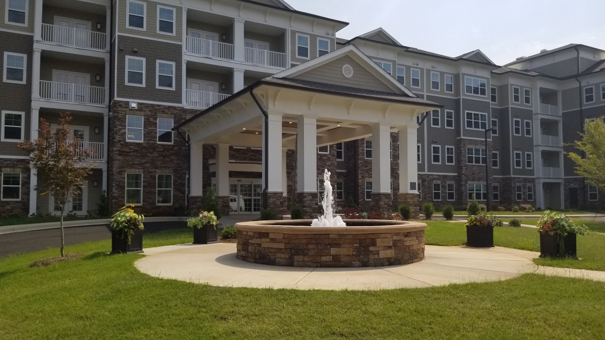 A modern building with a prominent entrance and a fountain in the front lawn.
