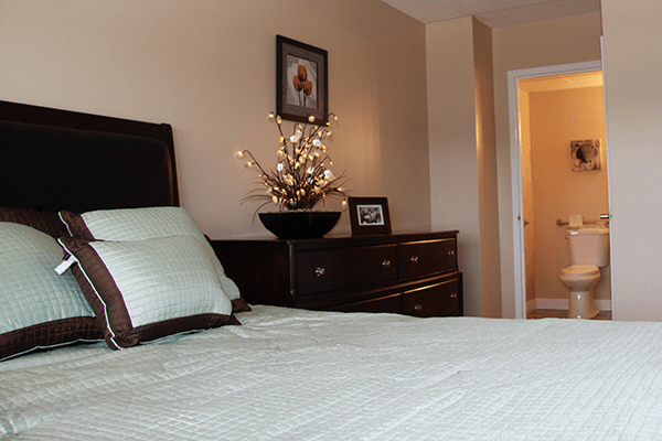 A cozy bedroom featuring a bed with soft pillows, a dresser with decorative elements, and artwork on the wall.