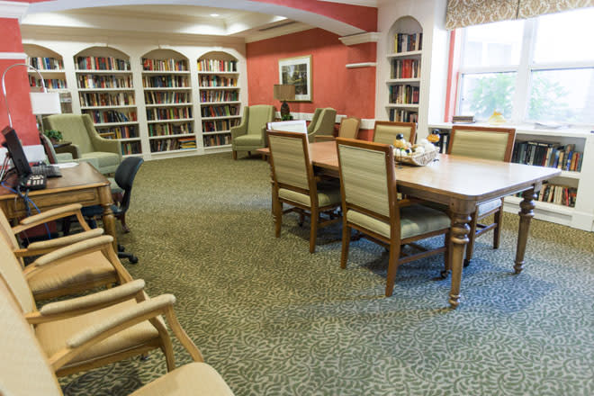 A cozy library with bookshelves, a large table, and comfortable chairs.