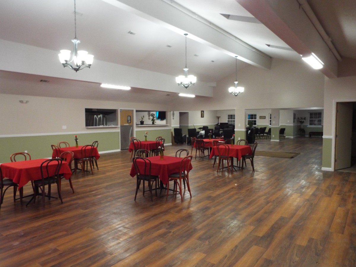 A spacious dining hall with tables covered in red tablecloths and wooden flooring.
