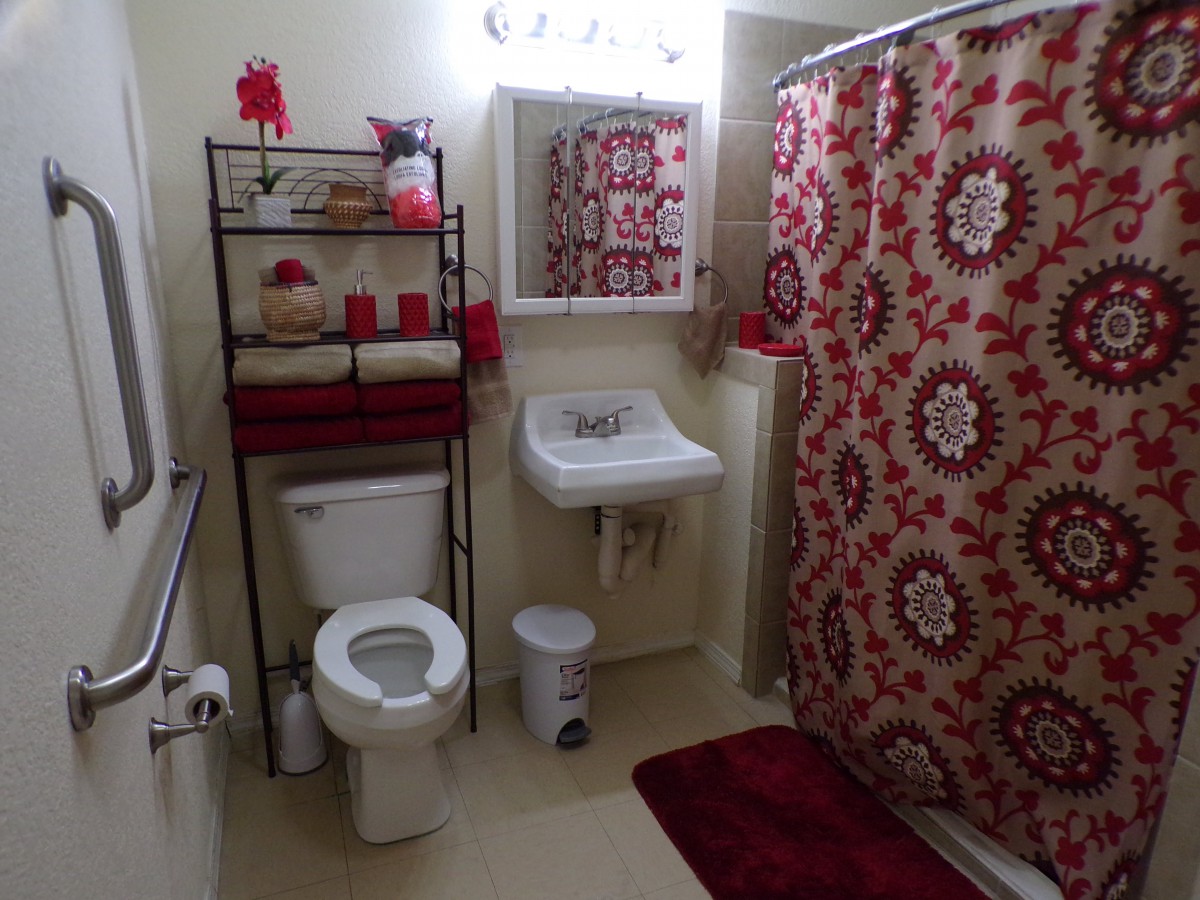 A neatly organized bathroom with red and floral decor.