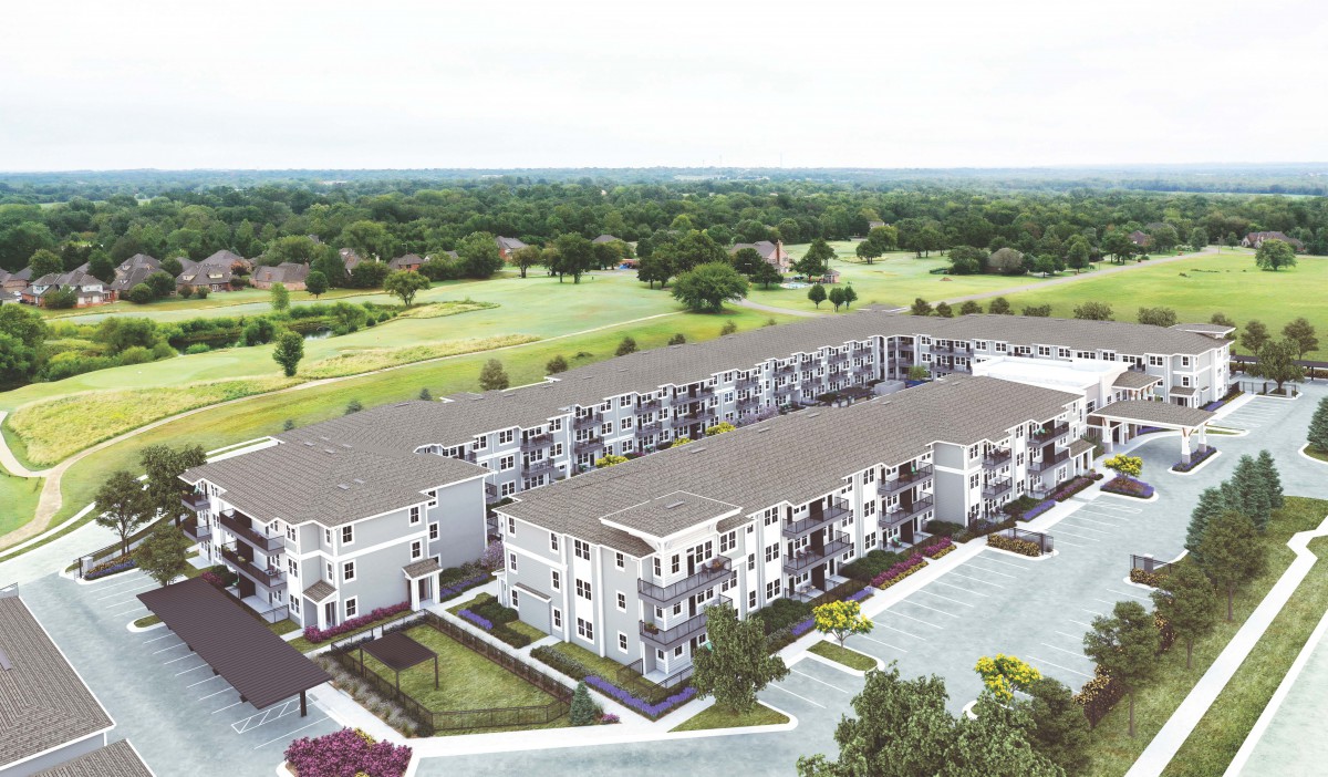 Aerial view of a suburban apartment complex with adjacent green landscape and parking area.