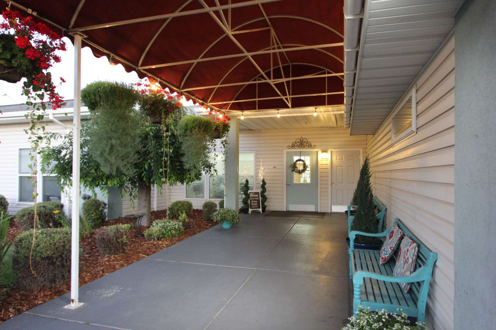 A cozy porch with a canopy, decorated door, and seating area surrounded by plants.