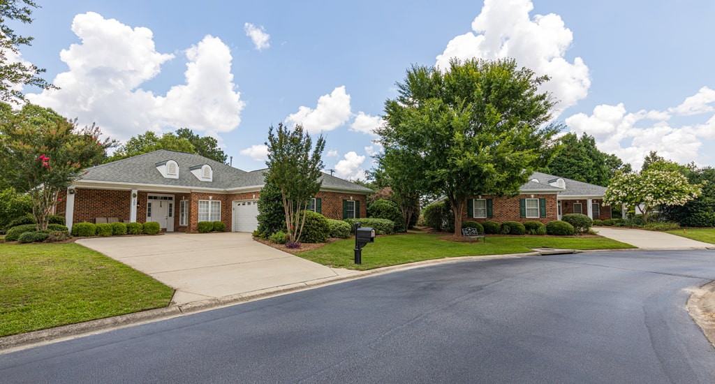A suburban house with a driveway and surrounding greenery under a cloudy sky.