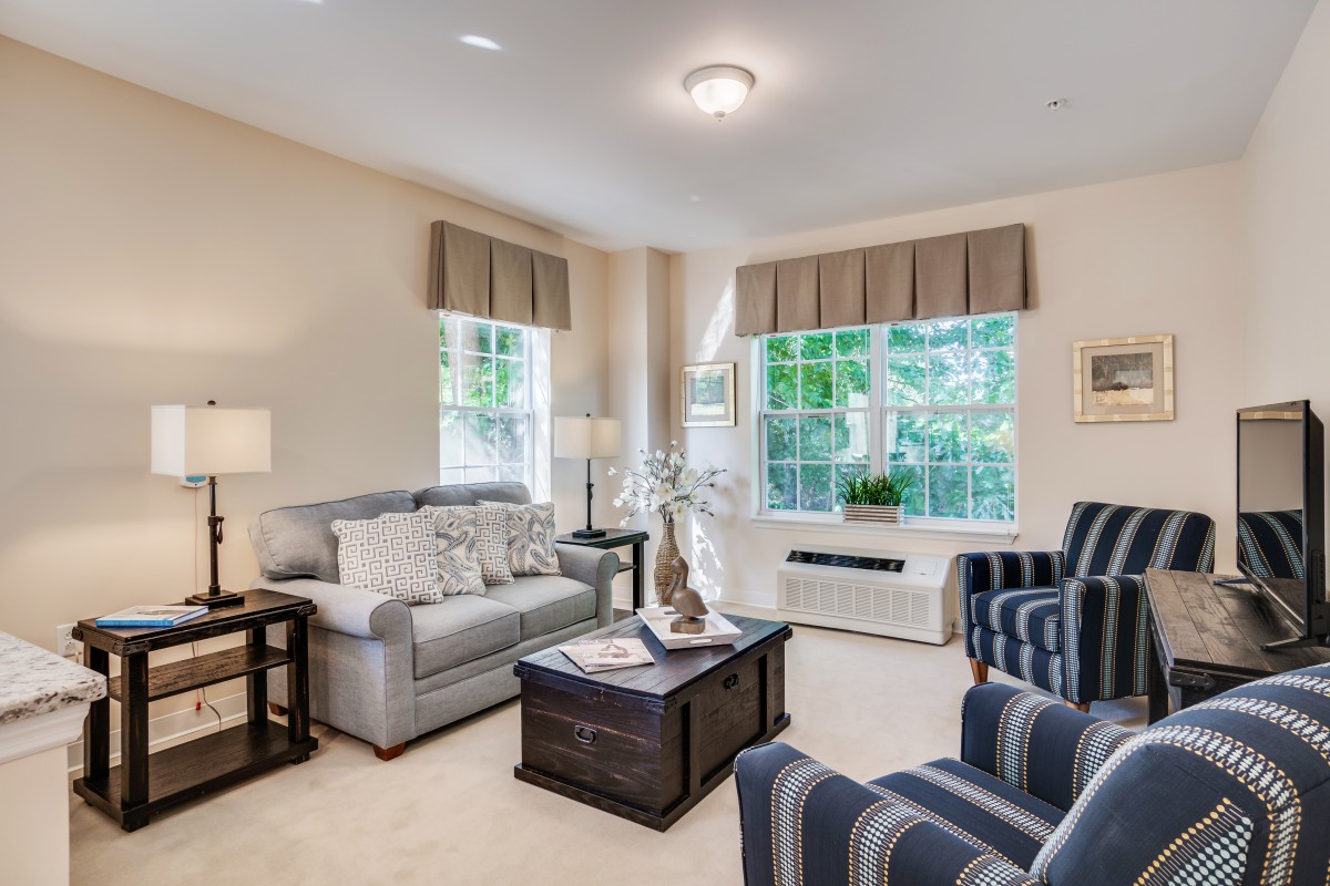 A cozy living room featuring a comfortable sofa, striped armchairs, and large windows with curtains.