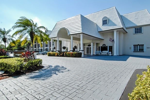 A modern building with a welcoming entrance, featuring palm trees and a paved driveway.