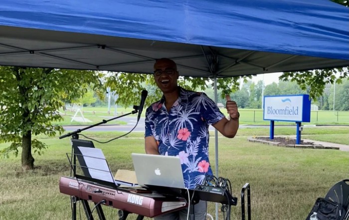 A musician performing outdoors under a tent with a keyboard and microphone.