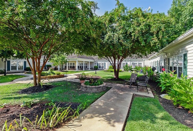 A lush garden with a pathway lined by trees and benches, offering a serene outdoor space.