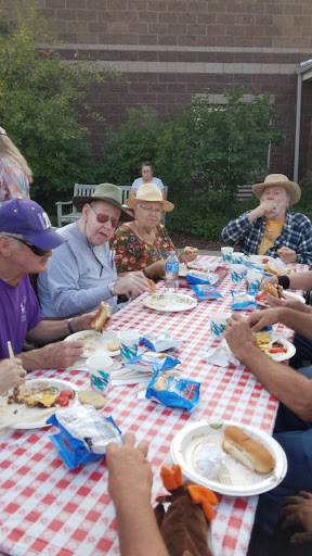 A cheerful outdoor gathering where senior citizens enjoy a meal together, surrounded by nature.