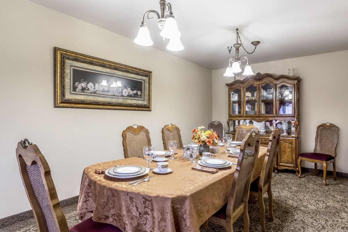 A well-set dining room table with a chandelier and china cabinet in the background.