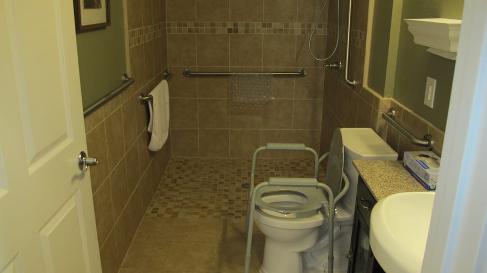 An accessible bathroom featuring grab bars and a handicap toilet frame for safety.
