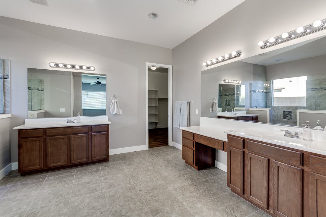 A spacious bathroom with double sinks and wooden vanities, featuring large mirrors and grey walls.