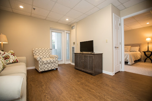 A cozy living room featuring a patterned armchair, modern TV stand, and warm wood flooring.