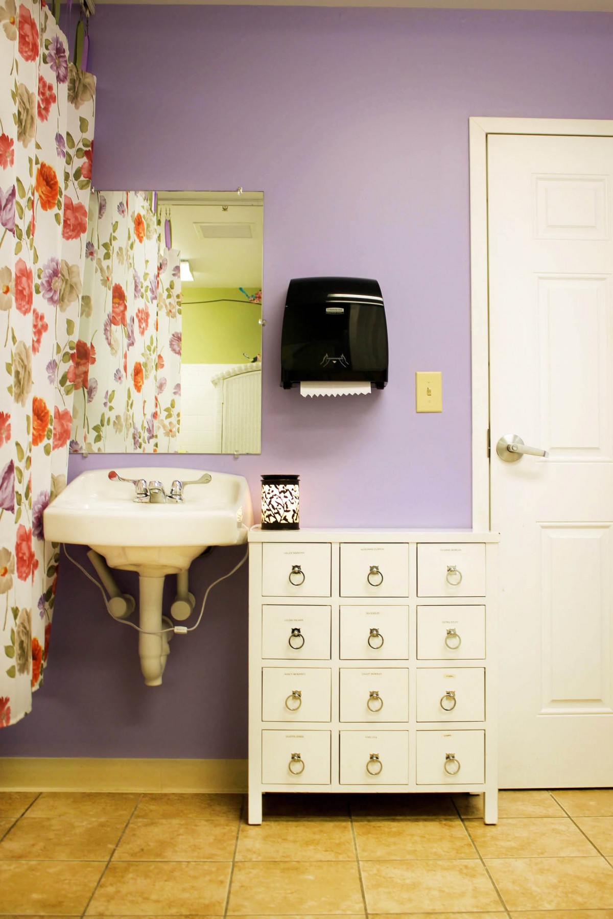 A brightly decorated bathroom with a floral shower curtain and storage drawers.