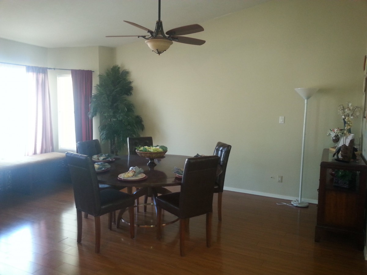 A cozy dining area with a round table and chairs on a hardwood floor, featuring a ceiling fan and a decorative plant.