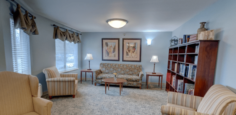A cozy living room featuring a patterned sofa, armchairs, coffee table, and floor lamps with artwork on the wall.